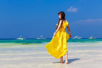 Fototapeta na wymiar Beautiful brunette woman in yellow dress with her back to the viewer on the tropical coast of the sea in a Sunny day. Summer vacation concept.