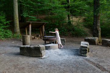 Girl playing in a white dress cooking at a fire place in the wood