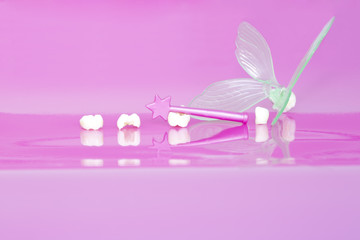 Milk teeth, tooth fairy wing and tooth fairy wand on rose background 