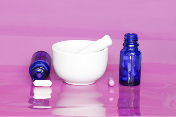 Mortar, pestle and capsules in blue glass containers on pink background