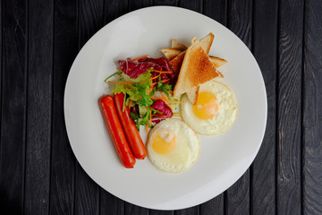 Top view of plate with fried eggs with sausages, salad and toast