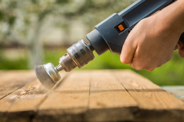Hands man with electrical rotating brush metal disk sanding a piece of wood