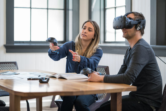 A woman delivers a presentation to a business colleague wearing a virtual reality headset.
