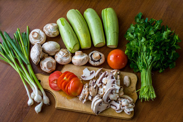 Raw vegetables and mushrooms on a wooden board cut for cooking.