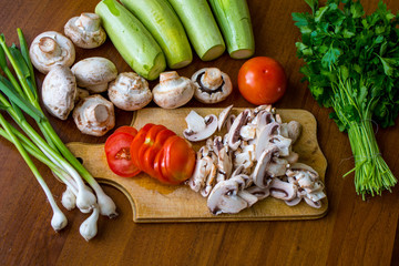 Raw vegetables and mushrooms on a wooden board cut for cooking.