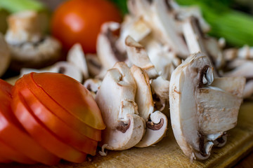 Raw vegetables and mushrooms on a wooden board cut for cooking.