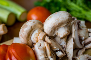 Raw vegetables and mushrooms on a wooden board cut for cooking.