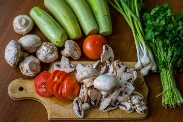 Raw vegetables and mushrooms on a wooden board cut for cooking.