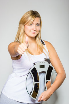 Happy woman holding weight machine showing thumb up