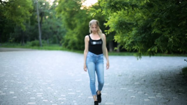 Young sexy blonde woman with very long hair is walking in the city park. Moves towards the camera