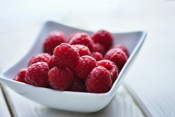Fresh and slightly imperfect raspberries in a white bowl on white board table