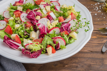 Fresh salad with mixed greens, radish, cheese and tomato in a plate on wooden background. Italian Mediterranean or Greek cuisine. Vegetarian vegan food