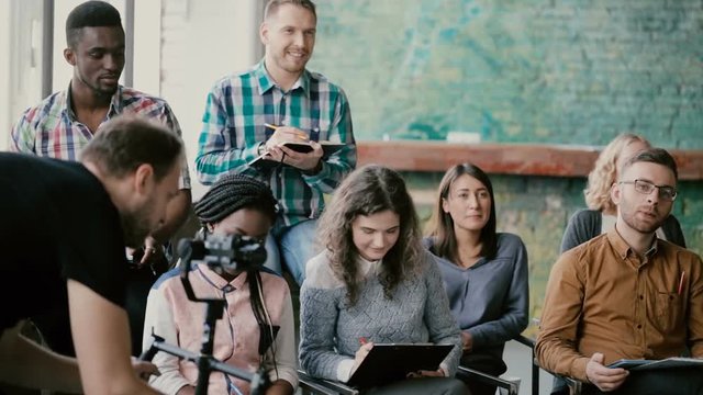 Mixed race group of people sitting together and listening business seminar. Man videograph with camera film the movie.