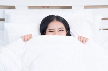 hiding under blanket. Woman smiling and looking aside.