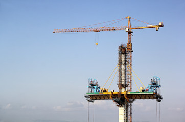 Deck of cable stayed bridge being erected on both sides of a tall concrete pier using tower crane for the third bridge across Mandovi River in Goa, India