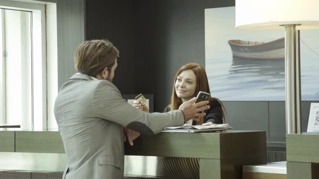 Businessman using credit card and smartphone to check in at hotel reception