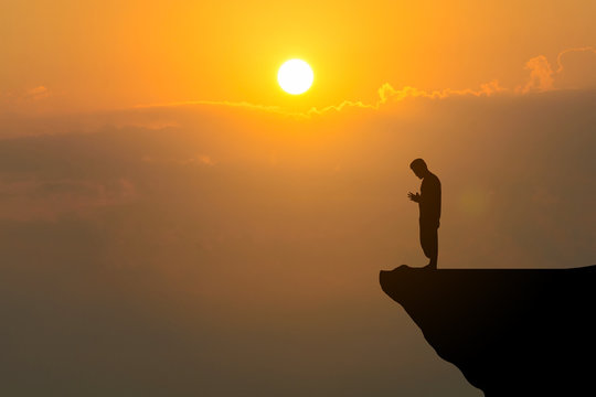 Man praying on cliff against sunset background