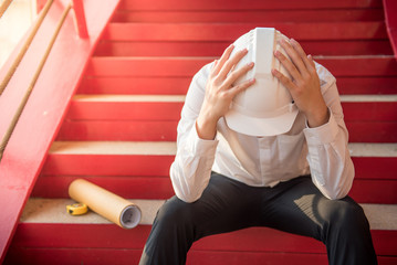 Engineer or Architect feeling tired and headache with his job. sitting on building stairs with...