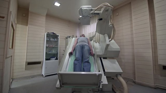 Middle aged male radiologist using scanner to performs x-ray imaging on younger man who lying on a machine at office, room interior, concept medical diagnostic, steady cam shot.