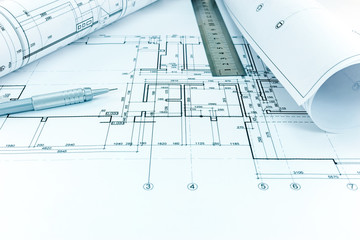 rolled blueprints, ruler and mechanic pencil on graphical architectural plan of a flat
