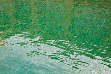 The Sun reflection on the green clear water ripples of swimming pool with mosaic floor.