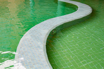 The Sun reflection on the green clear water ripples of swimming pool with mosaic floor.