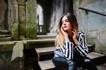 Fototapeta premium Fashionable woman look with black and white striped suit jacket, leather pants, posing at old street on iron stairs. Concept of fashion girl.