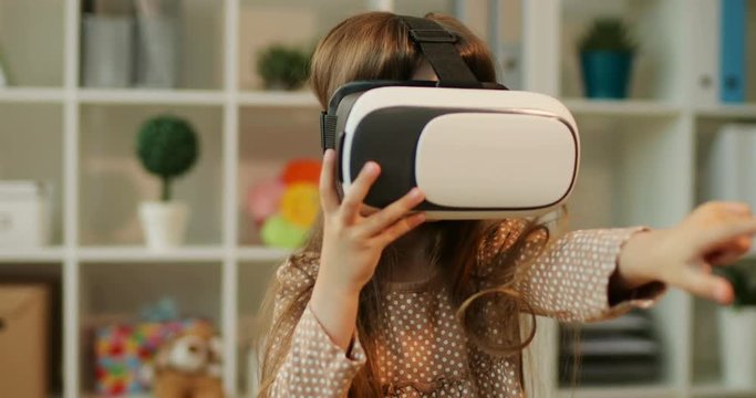 Caucasian pretty young girl with brown hair siting in home and playing the game using virtual reality glasses. Indoor.