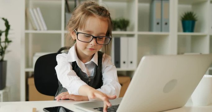 Young caucasian girl with glasses talking to camera. Girl siting at the desk in office video chatting with friend using laptop. Indoor.