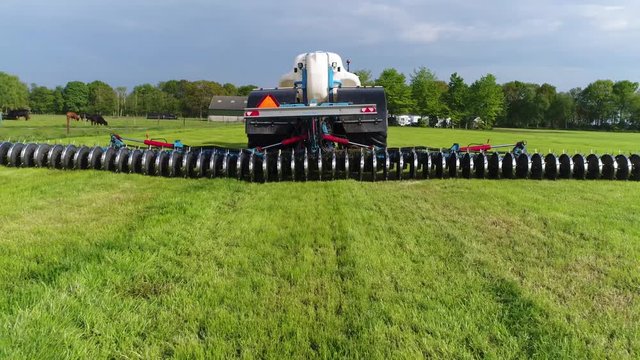 Aerial back view of farmer liquilising fertilizing grass field with specialized farming equipment made to improve and losening soil under grass big white trailer with liquid for getting soil wet