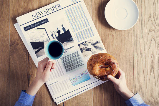 Female hands holding pastry with reading newspaper