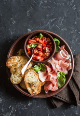 Italian antipasto - tomatoes bruschetta and prosciutto. On a dark background, top view. Delicious snack or appetizer for wine