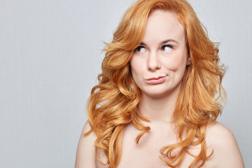 Naklejka premium I don't know.Headshot of doubtful Caucasian freckled female wearing nothing,but red long beautiful hair pouting lips and looking up with indecisive expression on her face, showing doubt and hesitation