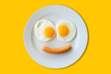 Smiling face frying eggs breakfast on a plate isolated yellow background.