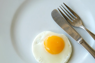 Top view of circle fried egg on white plate with knife and fork, serve for breakfast