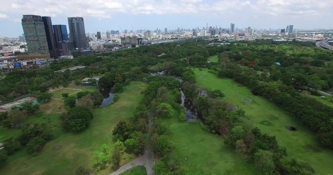 4K aerial shot of public park in Bangkok, Thailand in the morning with buildings.
