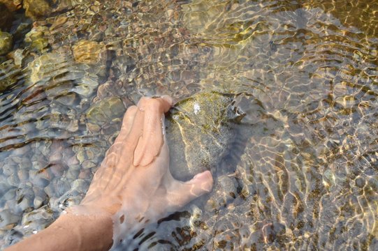 The hand that is taking the stone in the water