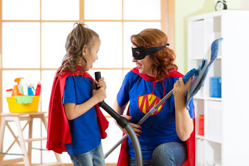Happy woman with kid cleaning room and have a fun. Mother and child girl playing together. Family in Superhero costumes.