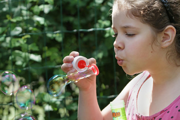 A teenage girl in a pink T-shirt concentrates blows soap bubbles. Soap bubbles as a model of the world economy