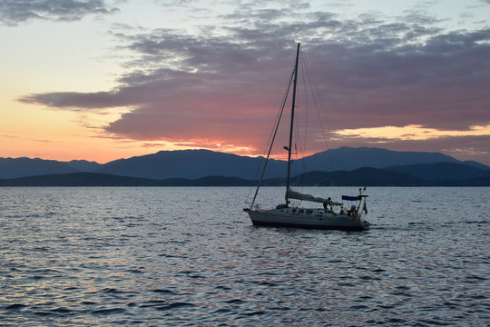 Silhouette of a yacht in the calm Ionian Sea near Corfu Island at dawn. The Albanian coast at horizon.