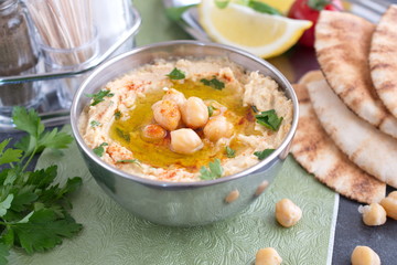 Chickpea paste with chick peas, garlic, cumin, sesami seads, olive oil, coriander in a metal bowl on a green cloth with pita bread and parsley. Traditional food. Healthy eating concept