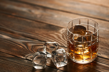 Glass of whiskey with ice cubes on wooden table