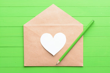 White sticker in the shape of a heart in an envelope on green wooden background