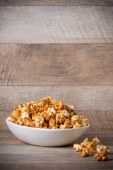 Caramel opcorn in bowl on the wooden table.