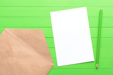 A blank piece of paper with an envelope on green wooden background
