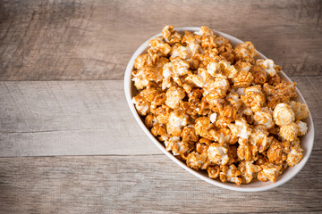 Caramel opcorn in bowl on the wooden table.