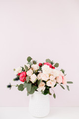 Beautiful flowers bouquet: bombastic roses, blue eringium, eucalyptus branches in flowerpot at pale pastel pink wall. Floral lifestyle composition.