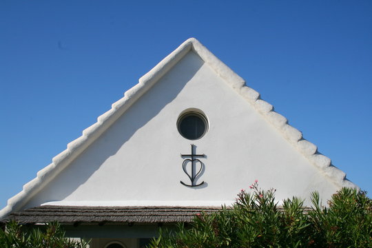 Croix de Camargue sur façade de maison blanche avec hublot