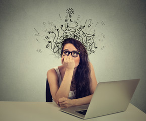woman with thoughtful expression sitting at a desk with laptop with arrows and symbols coming out of head