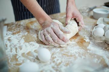 Hands of baker kneading dough on wooden board